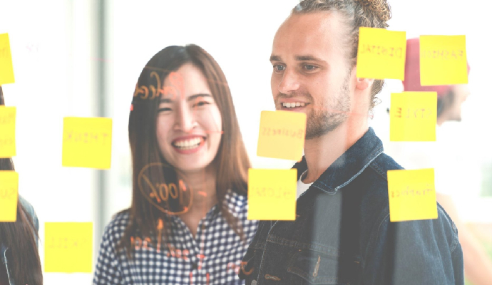  Diverse group of professionals in front of large, transparent presentation board covered with sticky notes